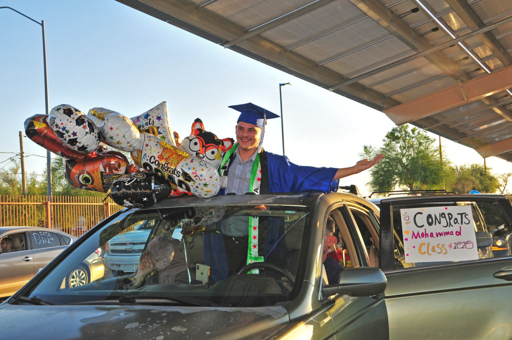 Graduate peeping out of car's moonroof holding a bunch of mylar balloons.
